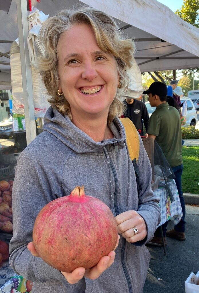 Peggy, holistic nutritionist holding a very large pomegrante.